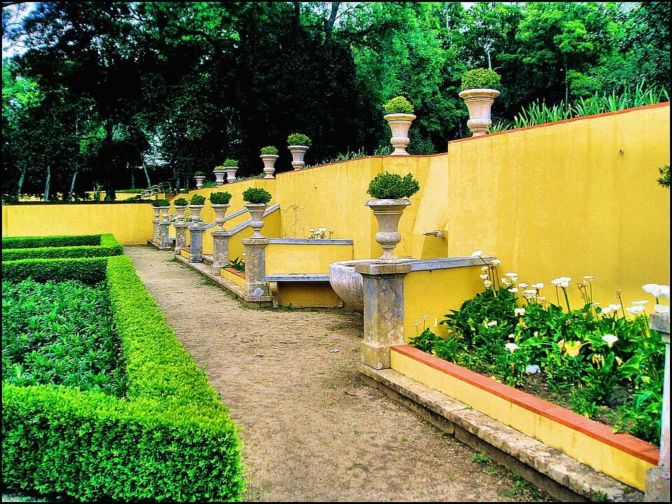 Canteiros geométricos, vasos e muro amarelo no Jardim do Cerco