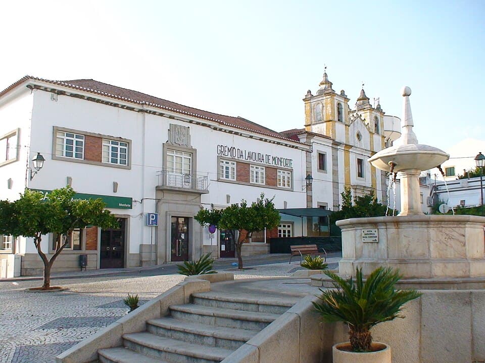 Praça da República de Monforte com fonte, edifícios e torres da igreja ao fundo