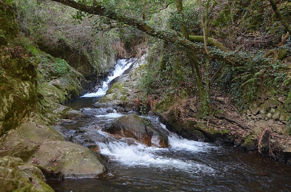 Queda de água entre rochas e vegetação no percurso da Pedra da Ferida
