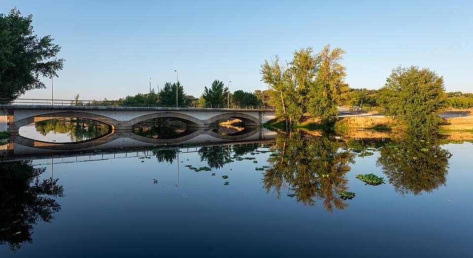 Ponte de arcos sobre a Ribeira de Sor refletida na água entre árvores