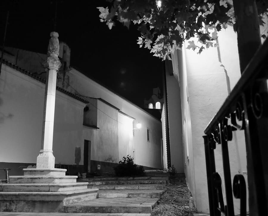 Pelourinho de Sousel iluminado à noite junto a edifícios brancos