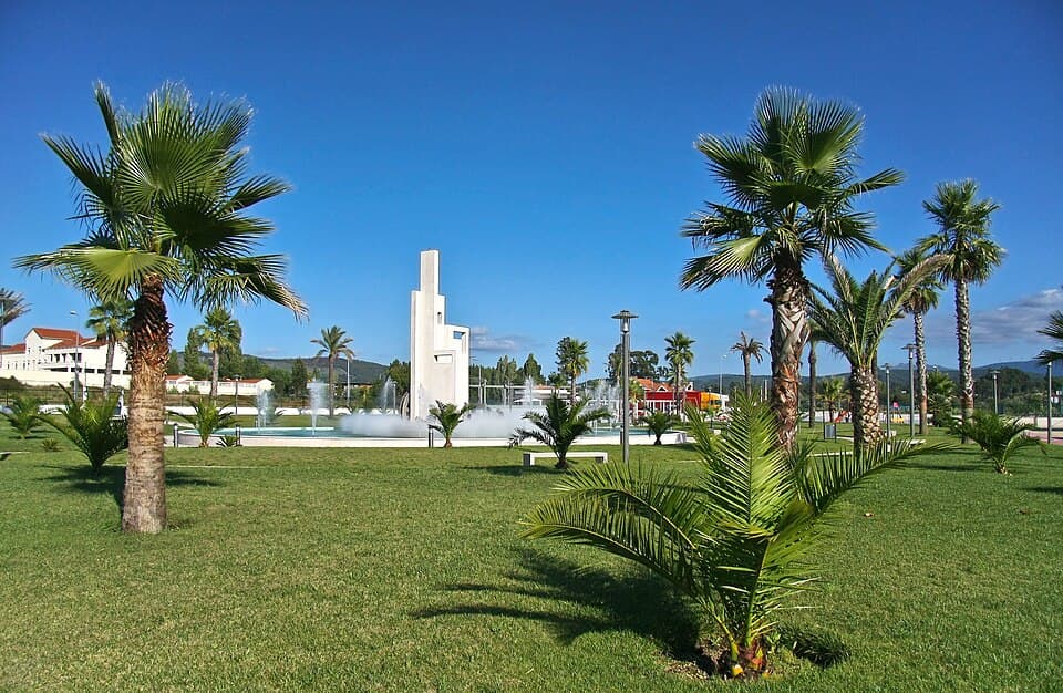 Palmeiras, relvado, fonte e monumento no Jardim à Raça Poiarense