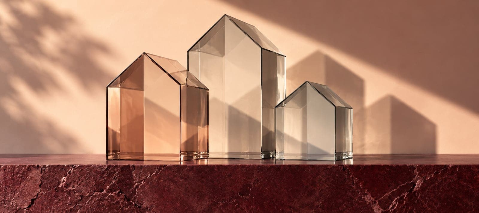 Ilustração gerada por IA de três volumes de vidro em forma de casa sobre uma prateleira em pedra bordeaux.