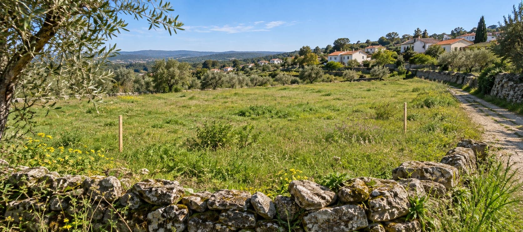 Ilustração gerada por IA de um terreno verde com estacas, muros em pedra, caminho e casas ao fundo; não representa um prédio ou uma autorização reais.